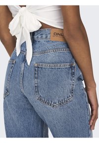 Jeans de tiro alto en azul claro con un parche de piel de la marca, que presentan bolsillos traseros clásicos y una textura ligeramente desgastada.