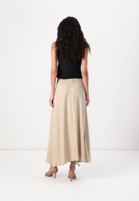 Falda ligera, beige y de longitud hasta el tobillo con un corte relajado y cinturilla elástica, combinada con una blusa negra sin mangas y tacones con tiras.