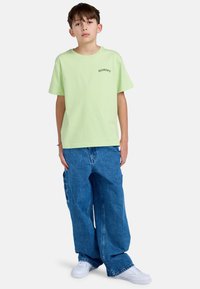 Lys grøn, kortærmet T-shirt med "ELEMENT" trykt i sort. Bæres med løse, blå denim bukser og hvide sneakers.