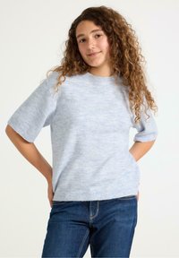 Lysblå strikket sweater med korte ærmer, rund halsudskæring og ribkant. Kombineret med mørkeblå jeans med synlige syninger.