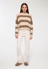 Sweter w paski w odcieniach beżu i brązu, luźny krój, tekstura prążkowana; zestawiony z białymi dżinsami i brązowymi zamszowymi półbutami. Prosta, casualowa stylizacja.