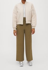 Ljusbeige bomberjacka med ribbade muddar och krage, i kombination med olivgröna vida byxor med en strukturell mönstring och dragkedjedetalj.