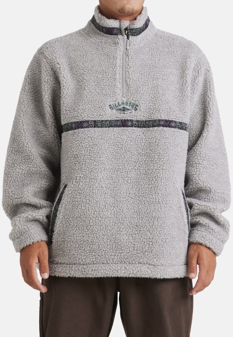 Lys grå fleecepullover med høj krave, halv lynlås, mærkeindbroderi og mønstrede accenter i sort, grøn og lilla. Har sidelommer.