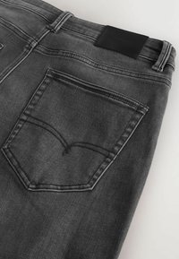 Jeans din denim gri cu o etichetă dreptunghiulară din piele neagră la talie, având buzunare din spate cu un model de cusătură curbat.