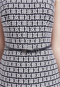Femme portant une robe à motifs floraux noirs et blancs avec une fine ceinture noire attachée autour de la taille.