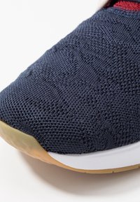 Chaussure de sport bleu marine avec dessus en maille texturée, semelle en caoutchouc et semelle intermédiaire blanche. Présente un motif subtil et une zone d'orteil renforcée.