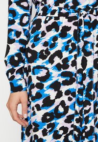 Kleid mit Leopardenmuster in Schwarz, Blau und Lavendel, mit langen Ärmeln und einem taillierten Gürtel, hergestellt aus leichtem Stoff.