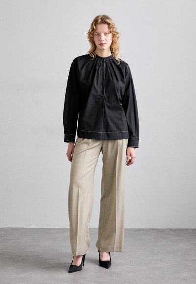 Top negro de manga larga con escote plisado y costuras en contraste, combinado con pantalones de pierna ancha beige y tacones de punta negra.