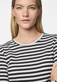Langsleeve geribbeld top met horizontale marineblauwe en witte strepen, voorzien van een ronde halslijn en subtiele textuur.