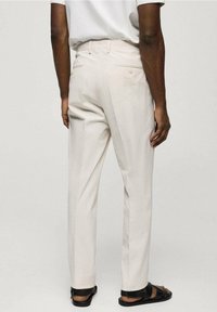 Svetle béžové kalhoty s jemným texturovaným vzorem, rovného střihu a zadními kapsami. Stylizováno s jednobarevným šedým tričkem a černými sandály.