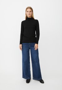 Jersey de punto negro de manga larga con cuello vuelto combinado con vaqueros anchos de mezclilla azul, con un diseño limpio y textura suave. Zapatos negros completan el conjunto.