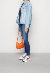 Chaqueta de mezclilla azul claro, camiseta negra, pantalones ajustados azul oscuro, zapatillas blancas y marino, y un pequeño bolso acolchado naranja.