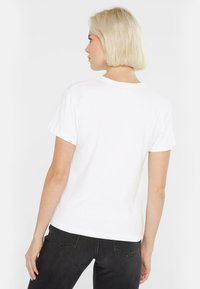 White cotton T-shirt with a relaxed fit, short sleeves, and a crew neckline, paired with dark denim jeans. Simple and classic design.