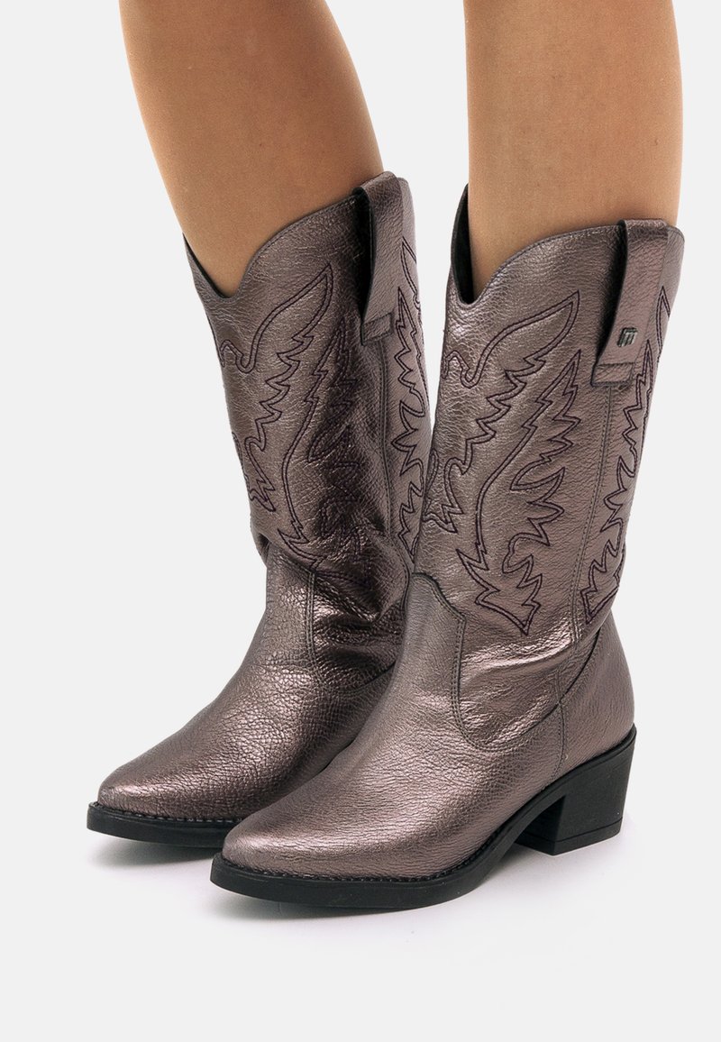 Botas de cowboy de bronce metálico con puntas puntiagudas, costuras decorativas y tacones ligeramente elevados. Fabricadas en cuero texturizado con un acabado suave.