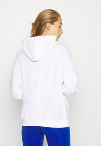 Hvit hettegenser med snor, oversized passform og ribbede mansjetter. Myk tekstur, kombinert med blå leggings.