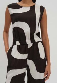 Mouwloze jumpsuit in zwart en wit, met gedurfde abstracte patronen. Elastische tailleband, zakken aan de zijkanten, zachte stoftextuur.