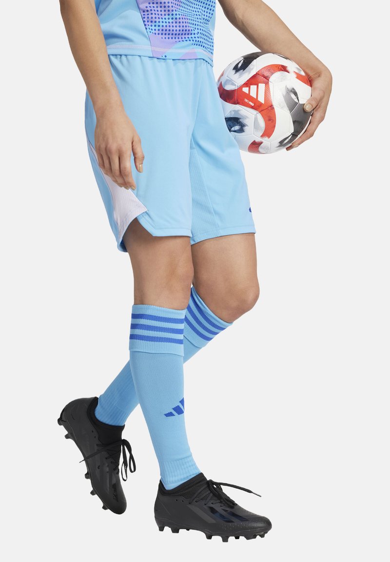 Licht blauwe voetbalshorts met een witte accent; zwarte voetbalschoenen; licht blauwe sokken met drie blauwe strepen; houdt een veelkleurige voetbal vast.