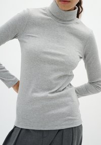 Pilkas juostelėmis turtleneck viršus, pagamintas iš minkštos medžiagos. Turi ilgas rankoves ir laisvai priglundančią konstrukciją, aukštą apykaklę ir subtilią tekstūrą.
