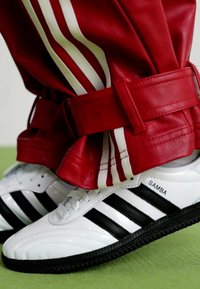 Hvite lær sneakers med svarte striper merket "SAMBA," kombinert med røde lærbukser med hvite sidestriper og et bredt belte.