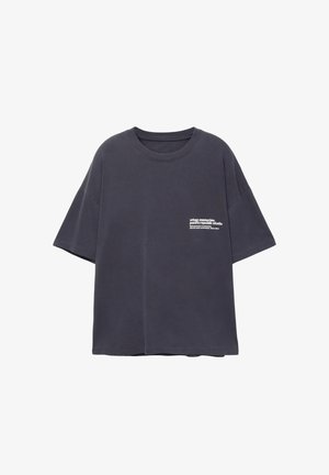 Sötét, túlméretezett pamut póló rövid ujjakkal. Az elején fehér szöveg található a bal mellkas részen. Egyszerű, sima dizájn minta nélkül.