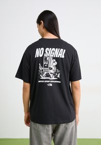 T-shirt en coton noir avec un design graphique "AUCUN SIGNAL" et un appareil en version cartoon, avec le texte "NE JAMAIS ARRÊTER D'EXPLORER" en dessous. Manches courtes.