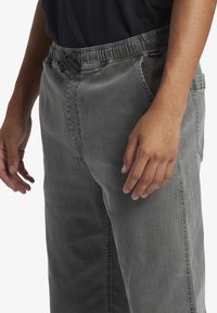 Gray denim pants with an elastic waistband, visible stitching, and side pockets. The fabric has a smooth texture and relaxed fit.