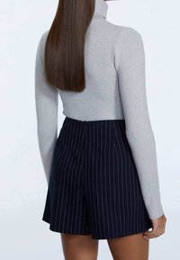 Grauer, langärmeliger Rollkragenpullover, kombiniert mit marineblauen, gestreiften Shorts, die ein tailliertes Design und einen Reißverschluss auf der Rückseite aufweisen.