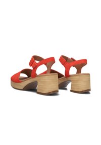 Rode suède hakken sandalen met open teen, uitsparingen en een verstelbare band. Voorzien van een gestapelde houten hak met horizontale groeven.