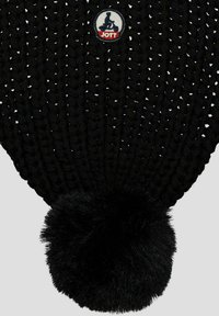 Gorro de punto negro con un diseño texturizado, que cuenta con un gran pompón de pelo sintético negro y un parche circular con el logo de JOTT.
