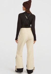 Beige sneeuwbroek met zwarte accenten, verstelbare banden en een relaxte pasvorm. Elastische taille en rits onderbenen voor gemakkelijk aan- en uittrekken.