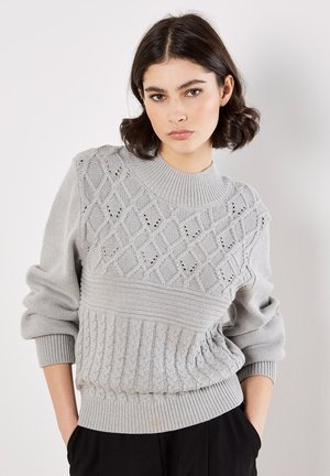 Maglione lavorato a maglia grigio chiaro con texture a trecce, fori a diamante sul petto e polsini e orlo a coste. Design classico con collo rotondo.