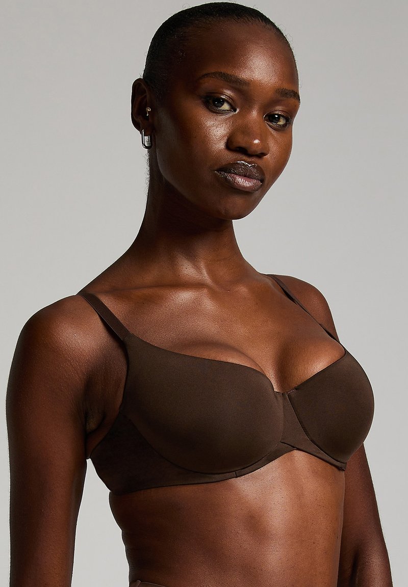 Bruine bh van soepel materiaal, met gevormde cups en verstelbare bandjes. Heeft een subtiele glans en een naadloos ontwerp voor comfort.