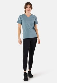 Lichtblauw sportt-shirt met een V-hals en korte mouwen, gecombineerd met zwarte legging en zwarte sportschoenen. Gladde, vochtregulerende stof.