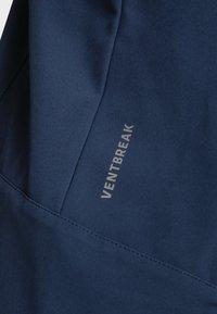 Námět modrá látka s hladkým povrchem, s úhlovými švy a nápisem "VENTBREAK" vytištěným ve stříbrné barvě.