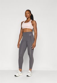 Světle růžový sportovní podprsenka a šedé legíny s vysokým pasem a bočními pruhy. Model má na sobě bílé sportovní boty. Hladká, elastická tkanina.
