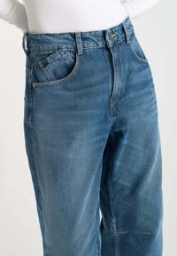 Blauwe denim jeans met een hoge taille, voorzien van twee voorkzakken, zichtbare naden en een relaxte pasvorm. De stof heeft een licht vervaagde textuur.