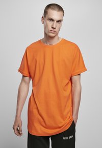 Tricou din bumbac portocaliu cu guler rotund, mâneci scurte și croială lejeră, asociat cu pantaloni negri care au text alb.