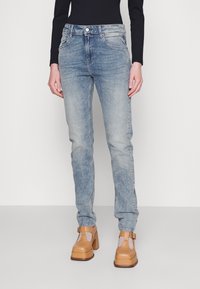 Vaqueros de mezclilla azul claro con un corte ajustado, cinco bolsillos y un acabado desgastado. Combinados con zapatos de plataforma marrones y una camiseta de manga larga negra.