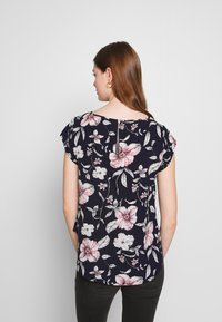 Blusa floral azul-marinho com mangas curtas, apresentando flores rosa e brancas. A parte de trás inclui um detalhe em forma de gota e uma bainha curva.