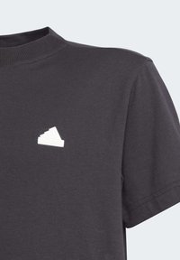 Camiseta de algodón gris oscuro con cuello redondo acanalado y un logo de Adidas blanco y texturizado en el lado izquierdo del pecho. Manga corta.