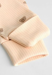 Ribbed fabric sleeves in soft peach color, featuring small brown teddy bear patterns. Textured material with cuffed ends.