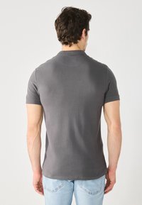 Grå polo skjorte med korte ærmer, glat tekstur og klassisk krave. Bæres med lyseblå jeans, som viser et enkelt og afslappet design.