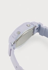 Lilla silikon klokke med firkantet kasse, to metallknapper og et teksturert armbånd med matt finish. Sølv metallbunn.