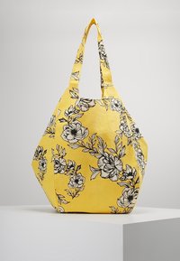 Borsa di stoffa gialla con motivo floreale nero, forma geometrica unica, due lunghe maniglie e superficie testurizzata.