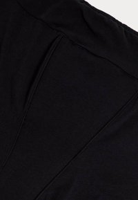 Tissu en coton noir avec une texture douce, présentant des coutures distinctes et un col rond. Design minimaliste, sans motifs ni accents visibles.