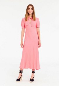 Robe midi rose avec des manches bouffantes et un col à nœud. Tissu lisse, jupe fluide, associée à des espadrilles bleu marine avec des liens noirs.