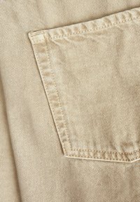 Tessuto beige con una trama diagonale testurizzata; presenta una tasca a toppa singola con cuciture rinforzate.