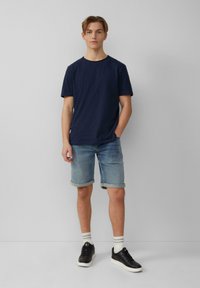 Donkerblauwe katoenen T-shirt met een ronde hals, gecombineerd met lichtblauwe denim shorts met een omgeslagen zoom. Gedragen met zwarte sneakers en gestreepte witte sokken.