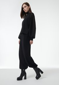 Zwart outfit met een gestructureerde, gebreide lange mouw top en bijpassende broek; gecombineerd met zwarte platform enkelboots. Eenvoudig, monochroom ontwerp.