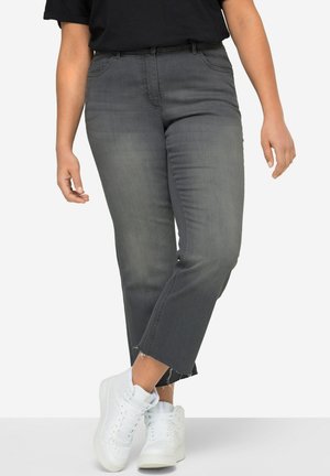 Jeans en denim gris avec une coupe droite, présentant un ourlet brut et des poches avant. Associés à des baskets montantes blanches.